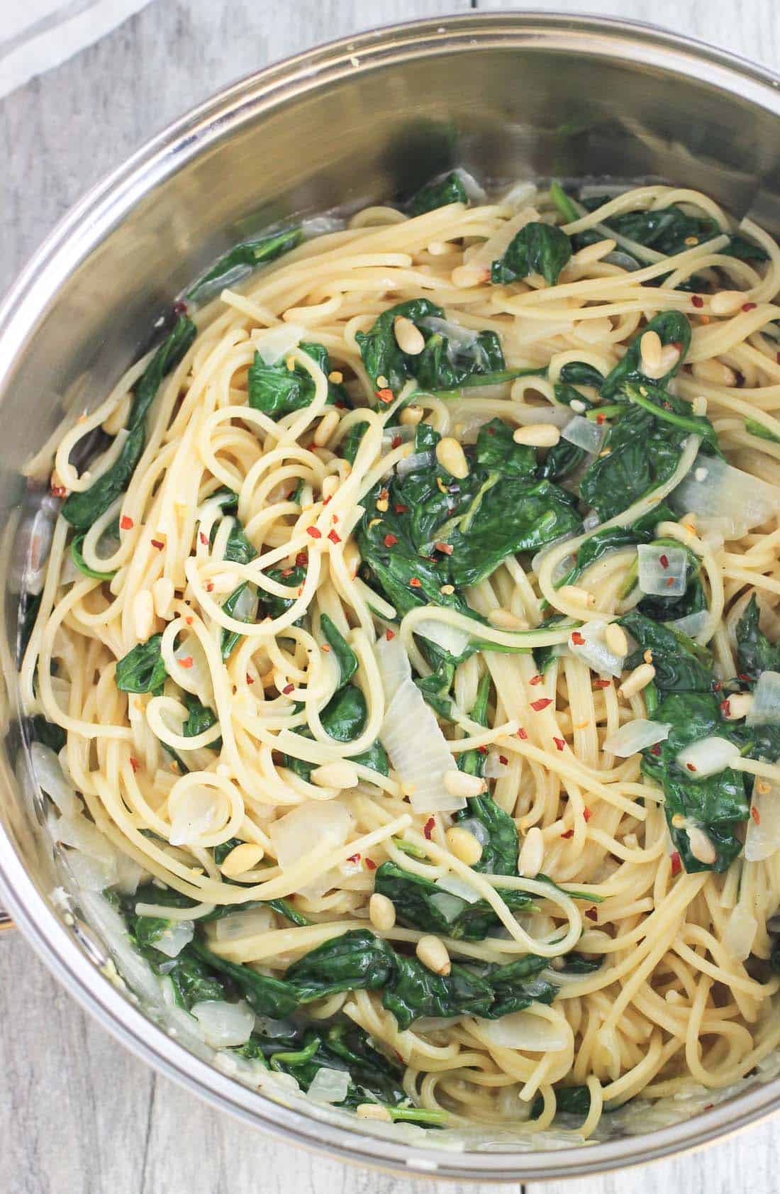 Pasta, spinach, sauce, and pine nuts cooked together in a large pot.