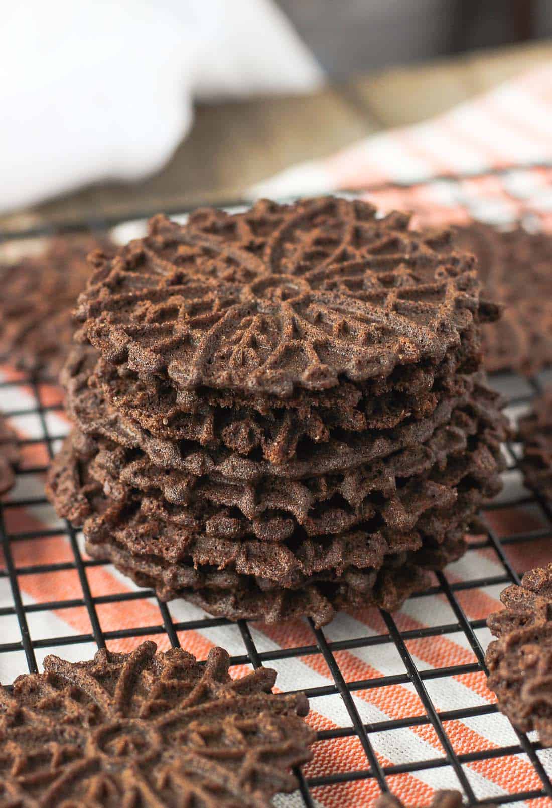 A stack of chocolate pizzelle on a wire rack.