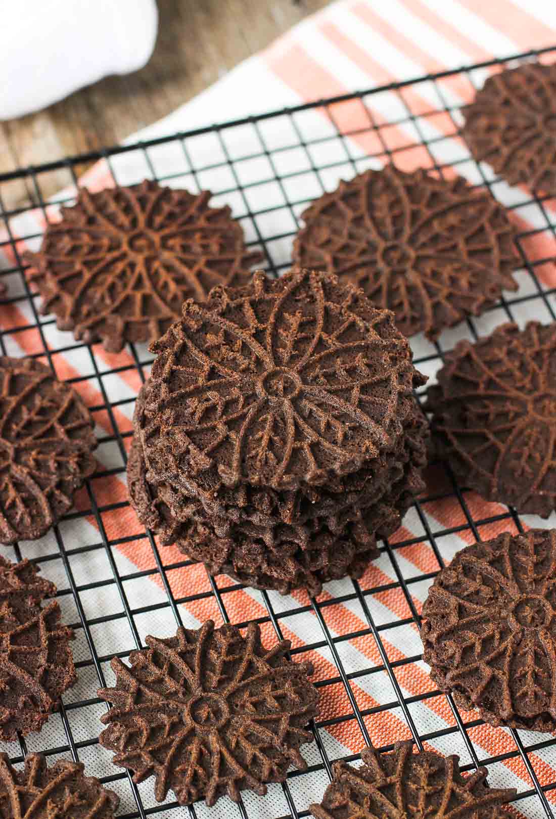 A stack of chocolate pizzelle on a wire rack.