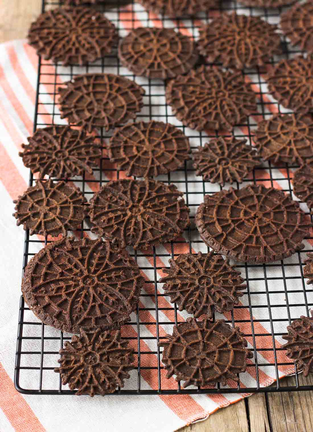 Chocolate pizzelle arranged on a wire cooling rack.