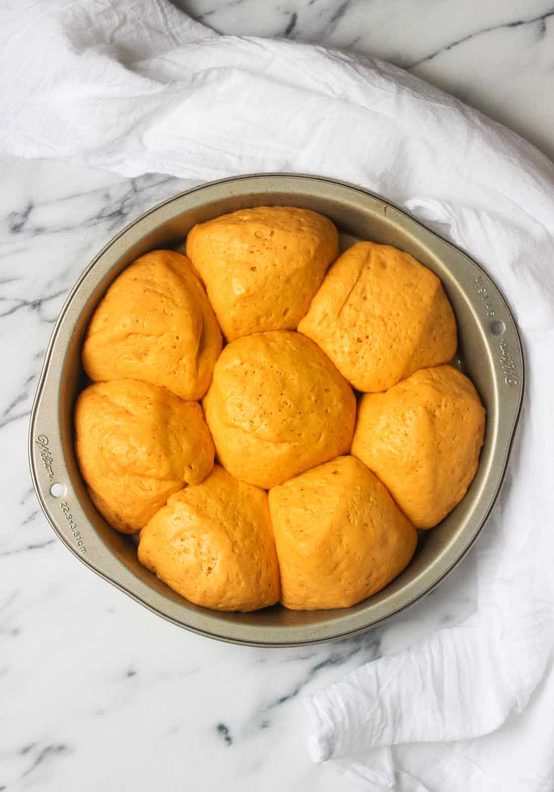 Risen rolls next to one another in a metal pan before baking.