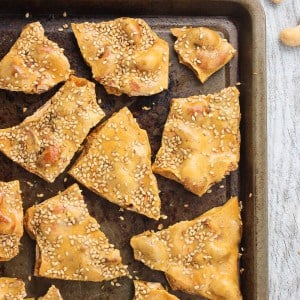 Broken pieces of cashew brittle on a metal baking sheet.