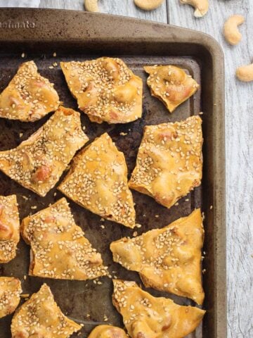 Broken pieces of cashew brittle on a metal baking sheet.