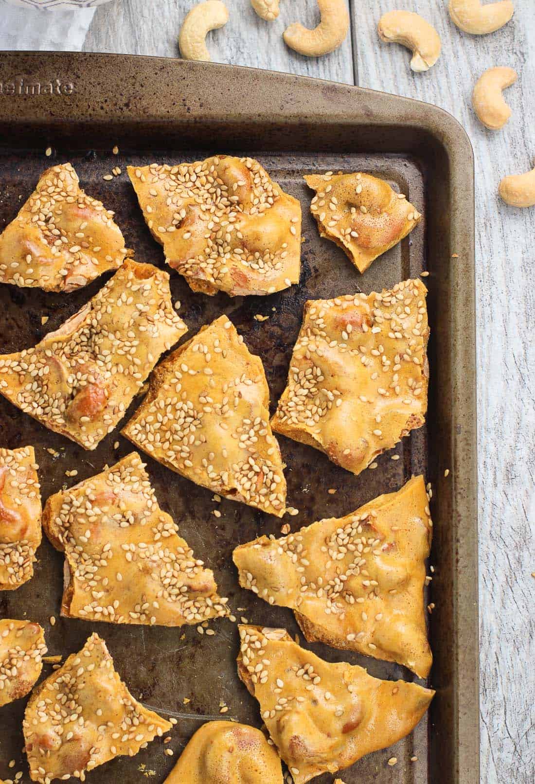 Broken pieces of cashew brittle on a metal baking sheet.