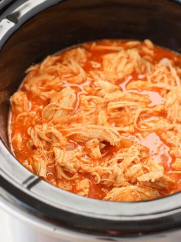 Shredded cooked chicken in buffalo sauce in a slow cooker.