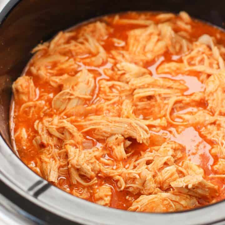 Shredded cooked chicken in buffalo sauce in a slow cooker.
