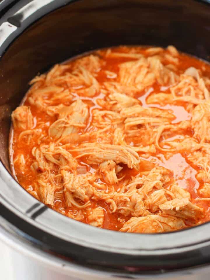 Shredded cooked chicken in buffalo sauce in a slow cooker.
