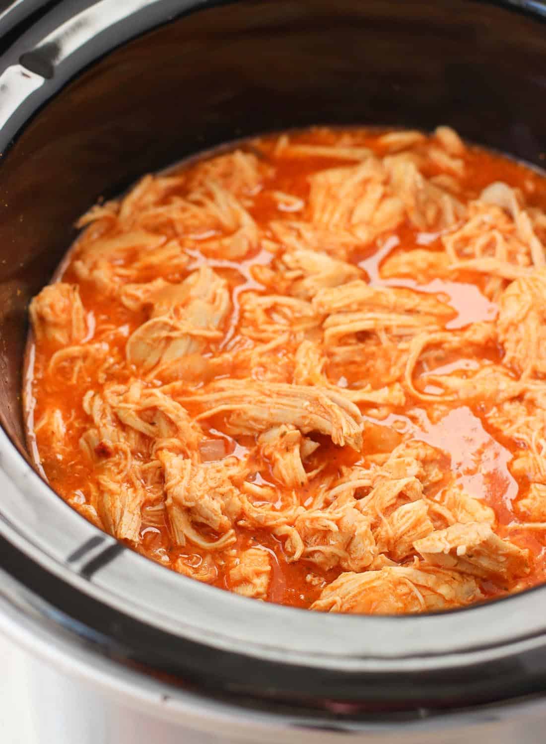 Shredded cooked chicken in buffalo sauce in a slow cooker.