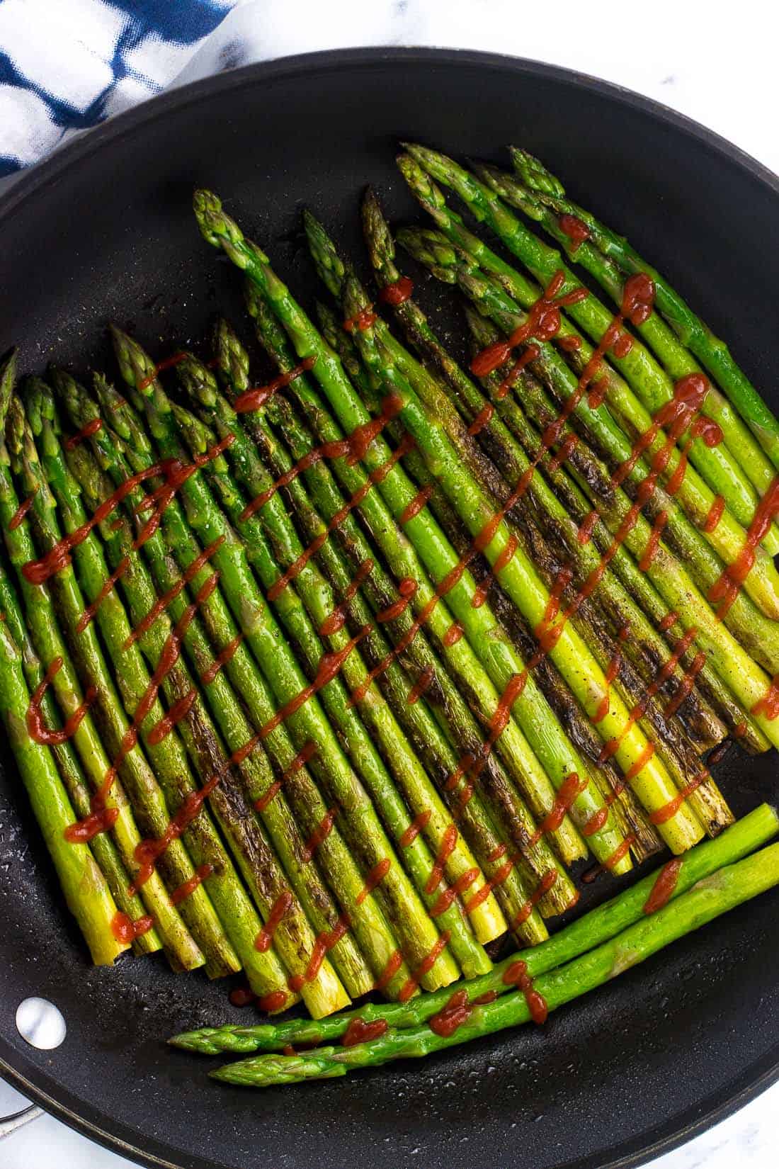 Asparagus in a large skillet drizzled with sriracha