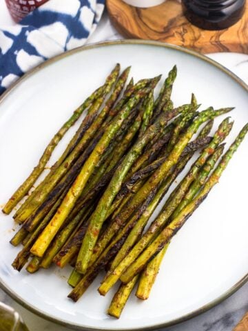 Sauteed asparagus on a serving plate after being roasted on the stovetop and seasoned with sriracha