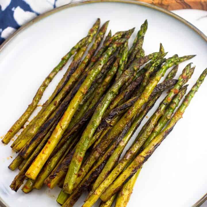 Sauteed asparagus on a serving plate after being roasted on the stovetop and seasoned with sriracha