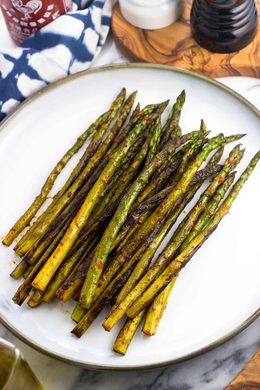 Sauteed asparagus on a serving plate after being roasted on the stovetop and seasoned with sriracha