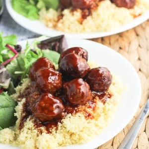 Two plates of salad and meatballs covered in sauce served over couscous.