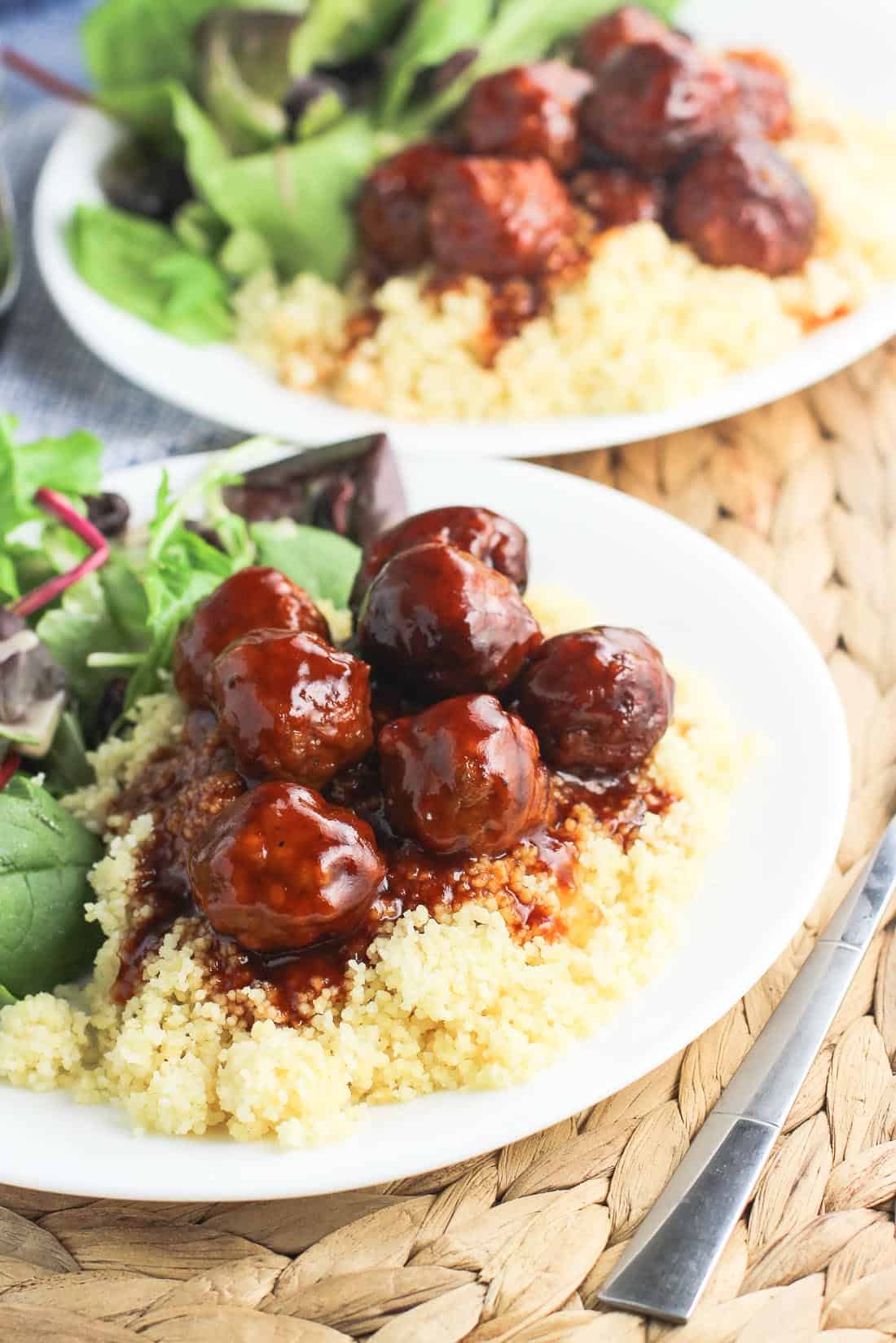 Two plates of salad and meatballs covered in sauce served over couscous.