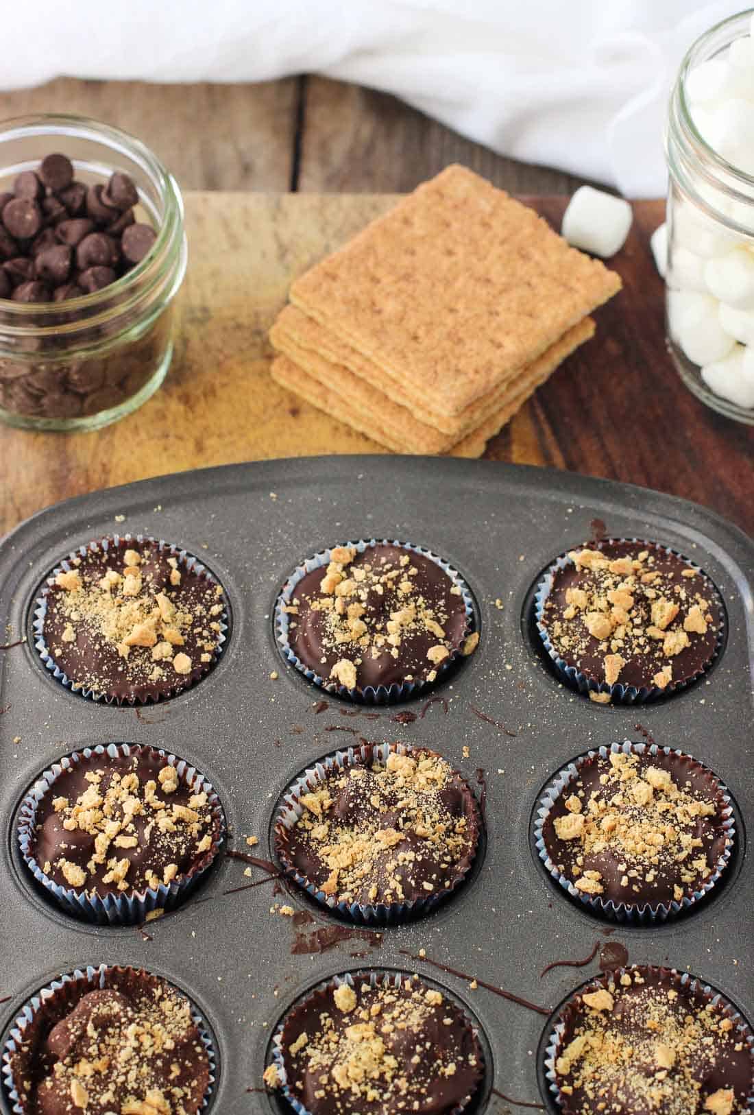 S\'mores cups in a metal mini muffin tin next to recipe ingredients.