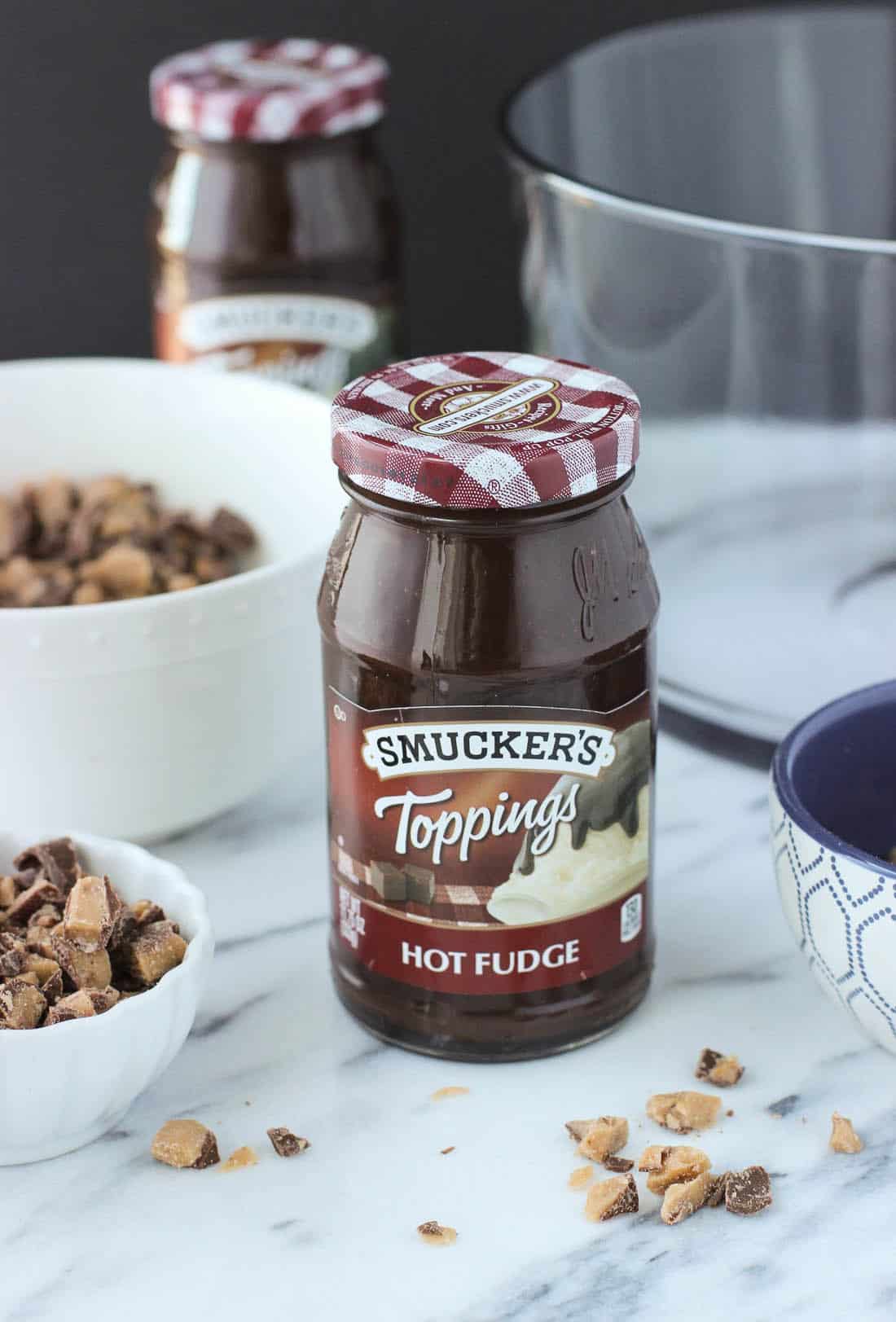 A jar of Smucker\'s hot fudge topping on a table next to the recipe ingredients.