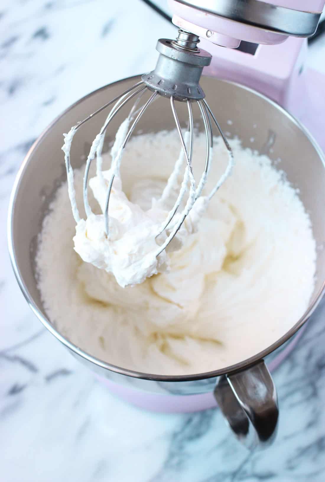 Whipped cream in the bowl of a stand mixer with the whisk attachment coated.