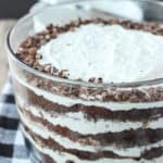 A large glass bowl filled with a layered mixture of cake, whipped cream, fudge, and toffee bits.