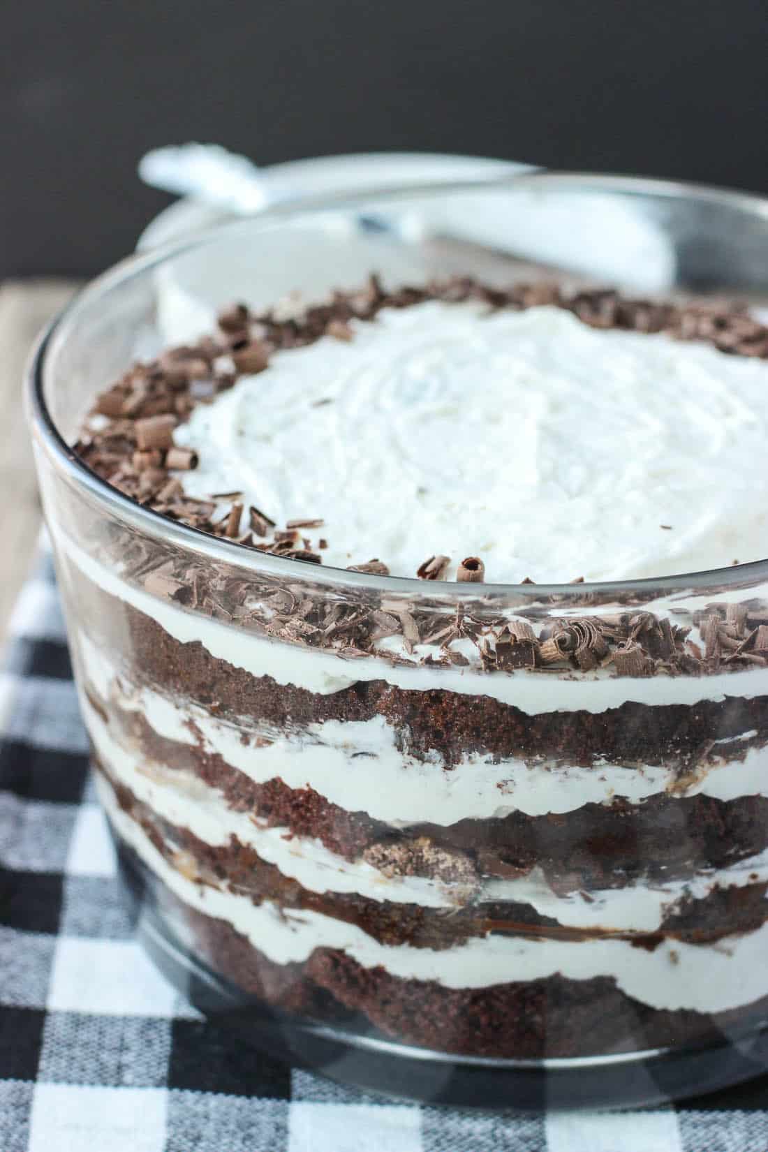 A large glass bowl filled with a layered mixture of cake, whipped cream, fudge, and toffee bits.