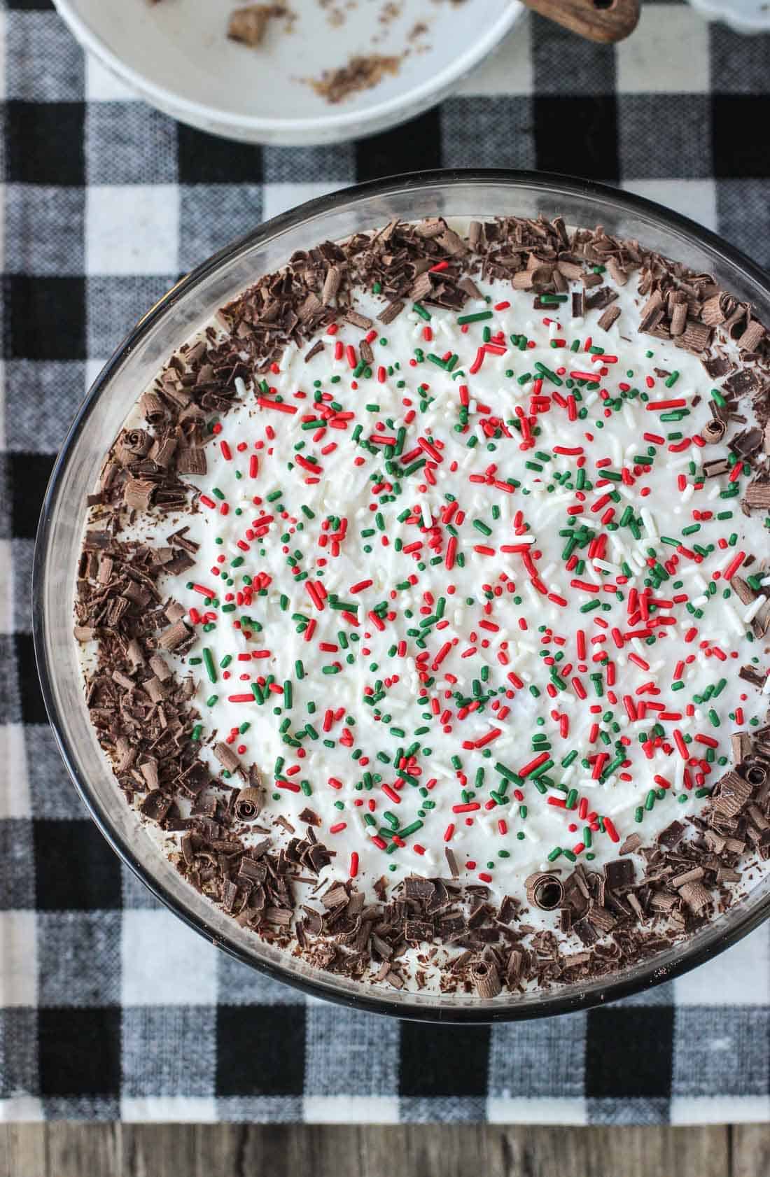 Trifle in a large glass bowl topped with Christmas sprinkles and chocolate curls.