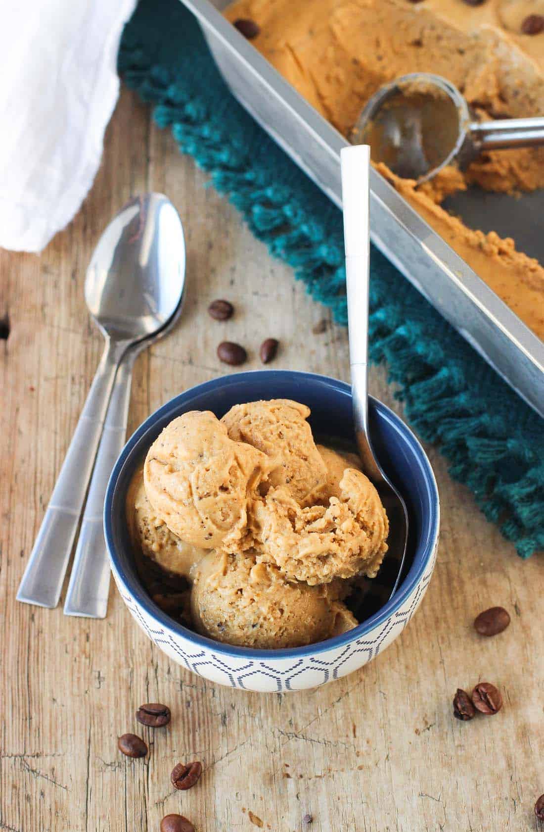 A bowl of vegan pumpkin ice cream with a spoon next to a metal carton of it