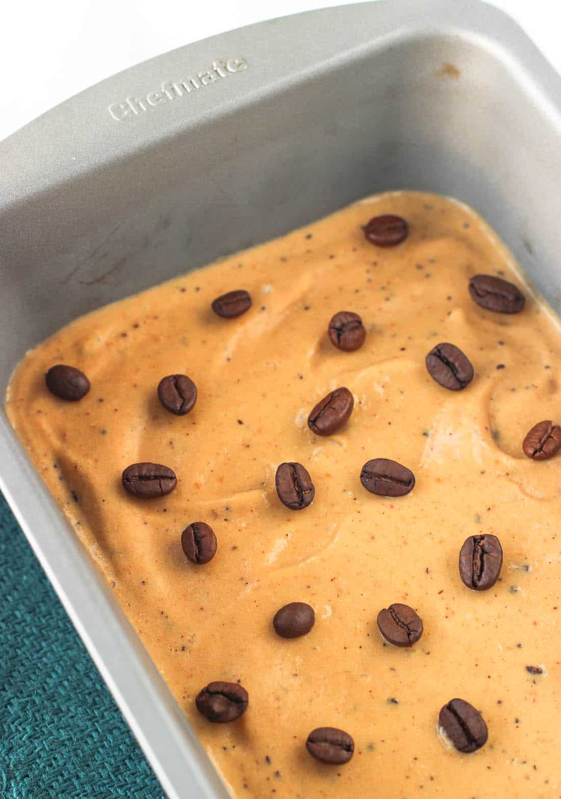 Freshly churned ice cream in a metal loaf pan with whole espresso beans added to the top