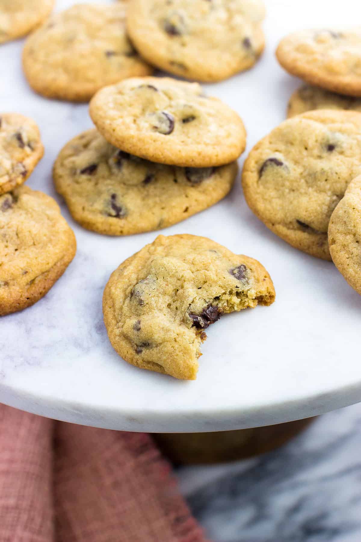 Cookies on a marble top cake stand with the front cookie having a big bite taken out.