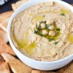 A bowl of hummus on a plate of pita chips.