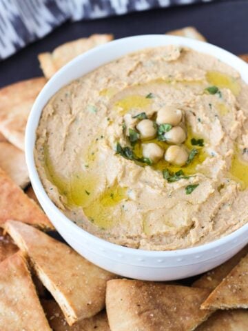 A bowl of hummus on a plate of pita chips.