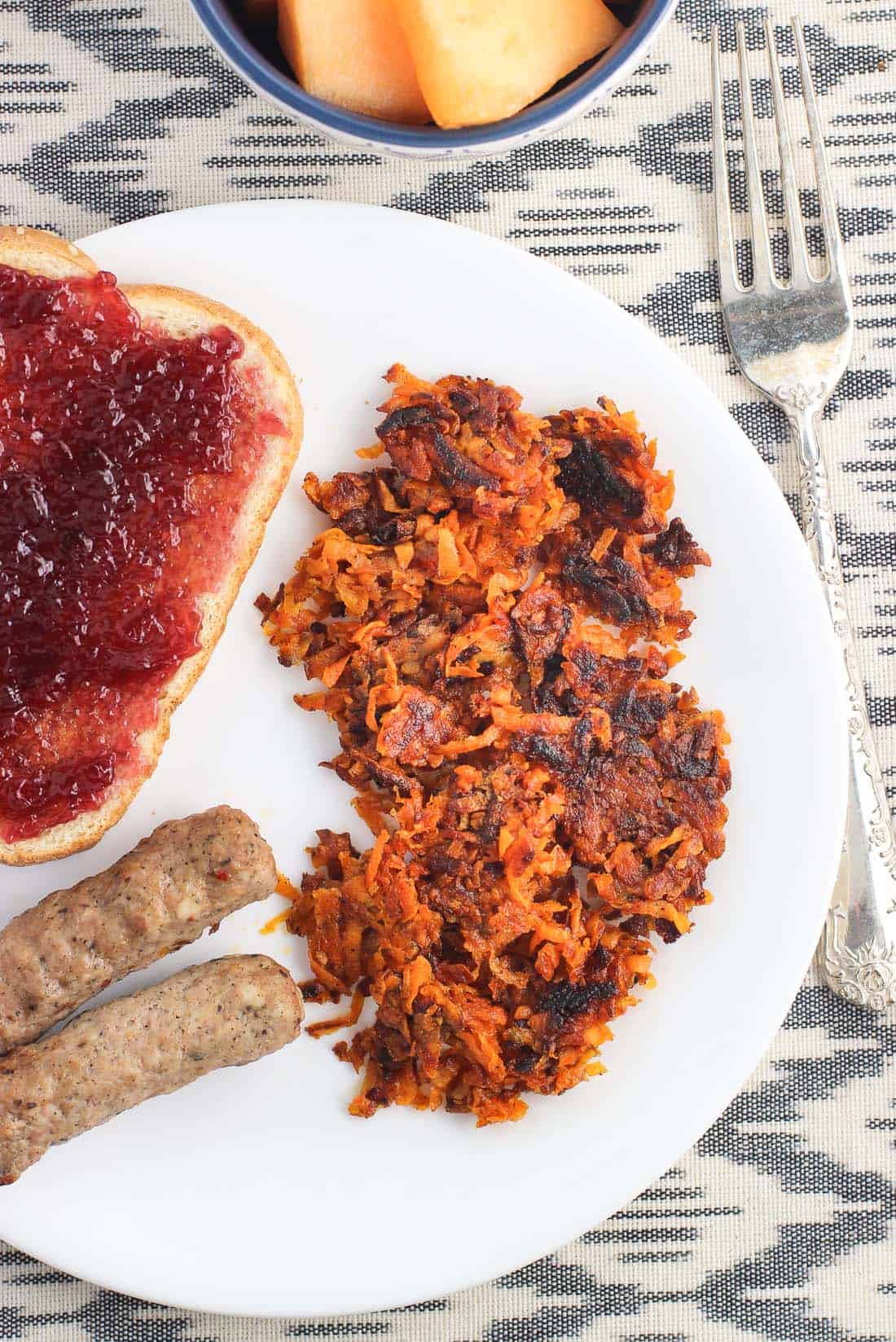 A plate with sausage links, toast with jelly, and sweet potato hash browns.