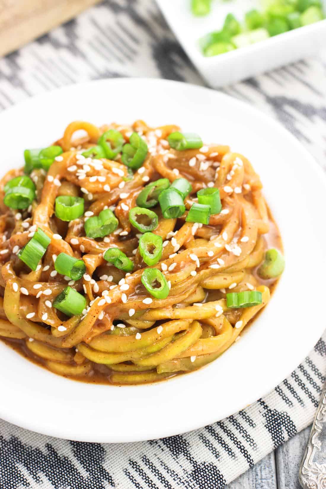 A plate of zoodles in sauce topped with green onion and sesame seeds.