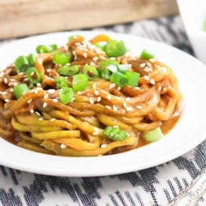 A plate of zucchini noodles in sauce topped with sliced green onion.