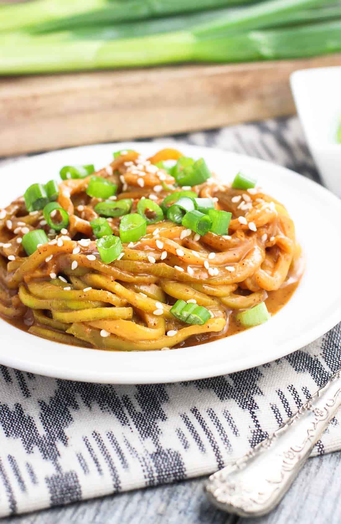 A plate of zucchini noodles in sauce topped with sliced green onion.