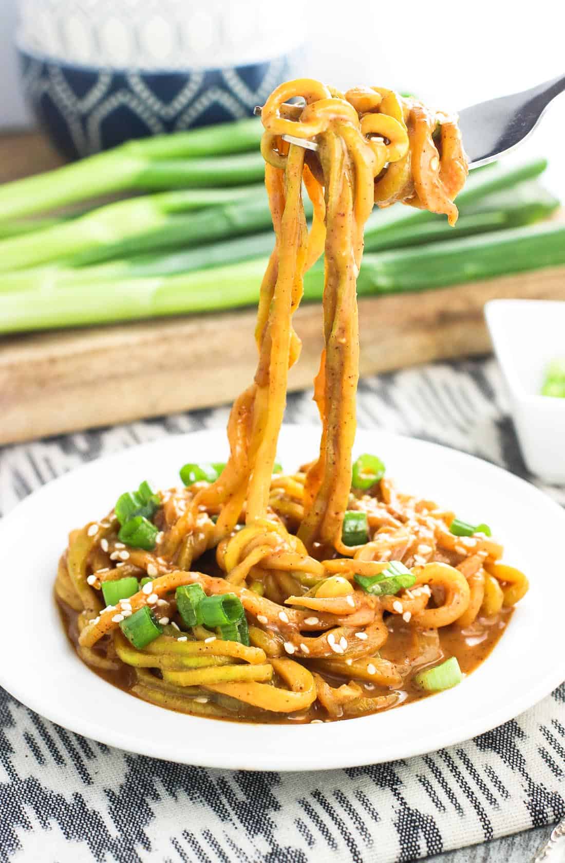 A fork lifting zucchini noodles in sauce off of a plate.