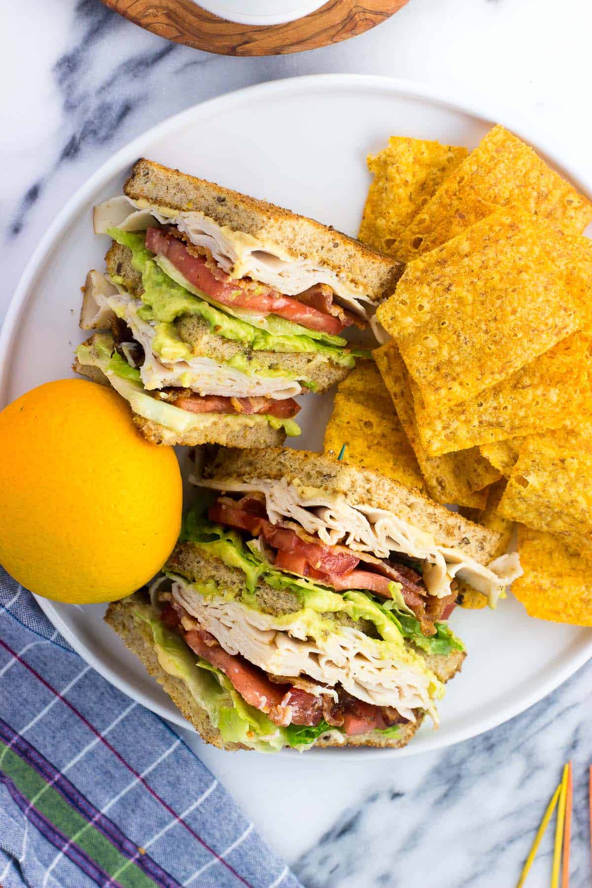 The sliced sandwich on a plate with an orange and chips.