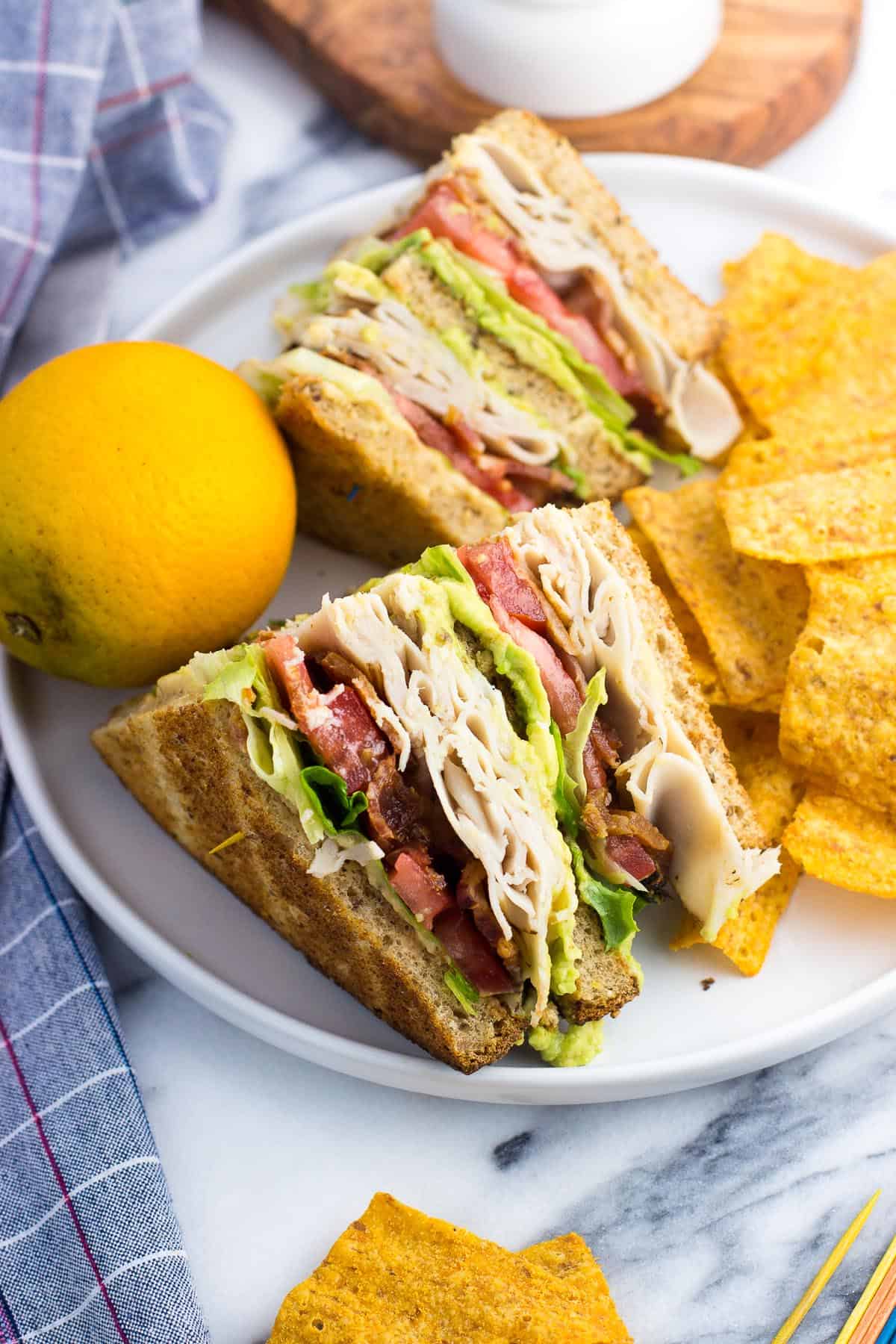 Two sandwich triangles on a plate with an orange and chips.