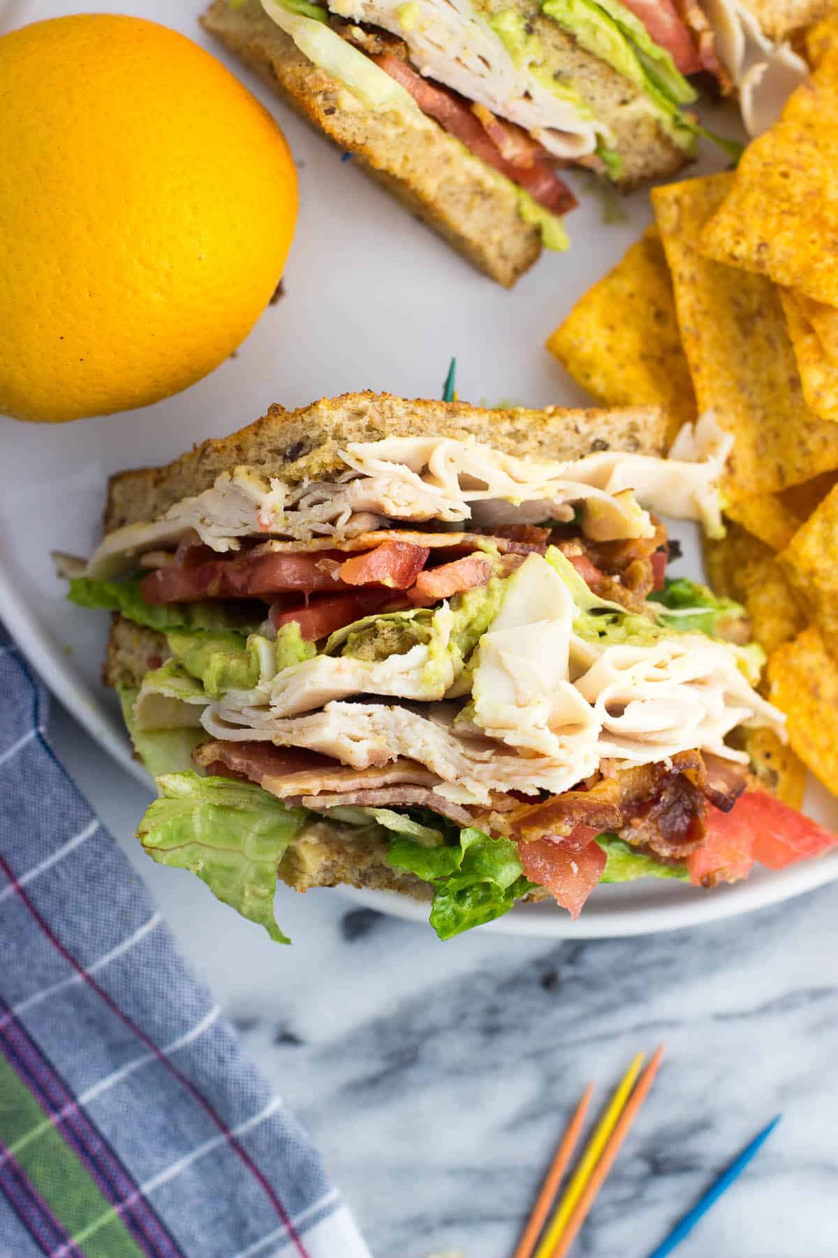 An overhead view of one sandwich half on a plate with chips and an orange.