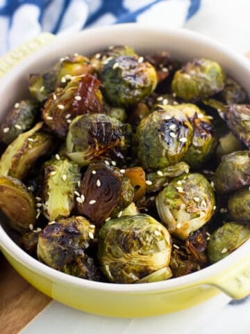 A small shallow dish filled with roasted brussels sprouts topped with sesame seeds in front of a dish towel