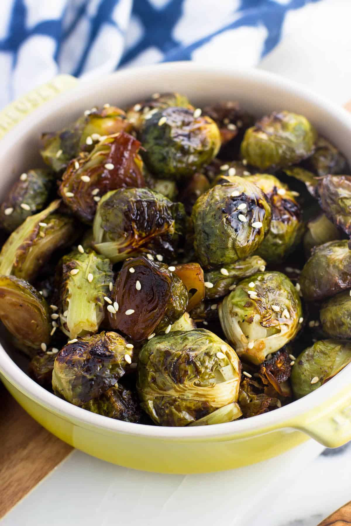 A small shallow dish filled with roasted brussels sprouts topped with sesame seeds in front of a dish towel