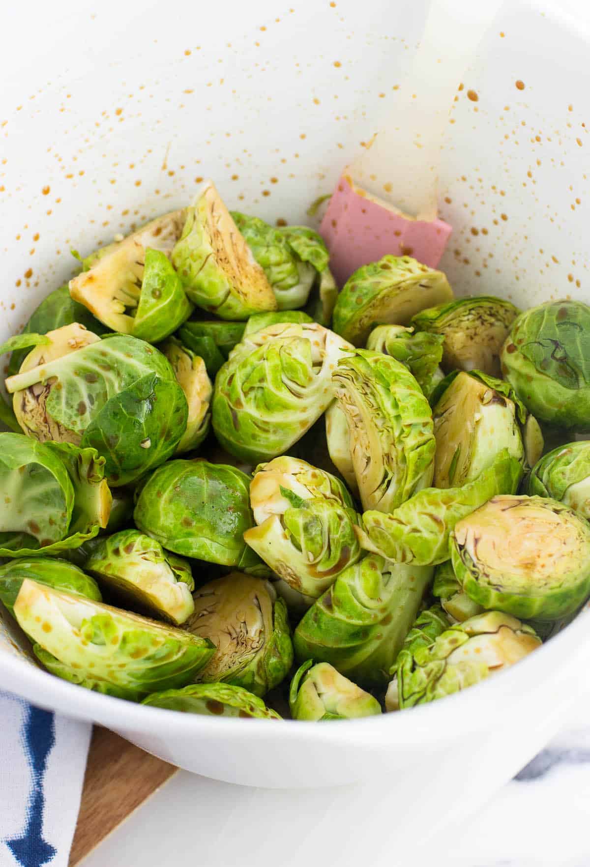 Halved brussels sprouts tossed in honey and other ingredients in a large plastic mixing bowl with a spatula