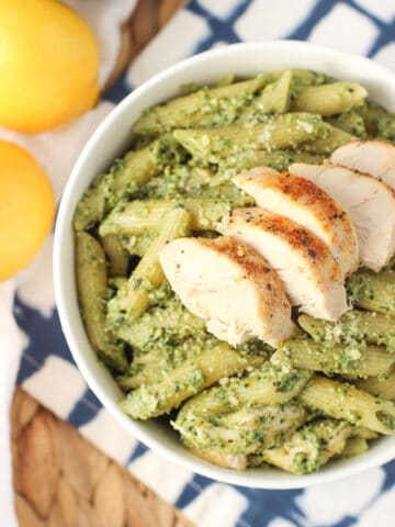 A bowl of pesto pasta with cooked chicken on top.