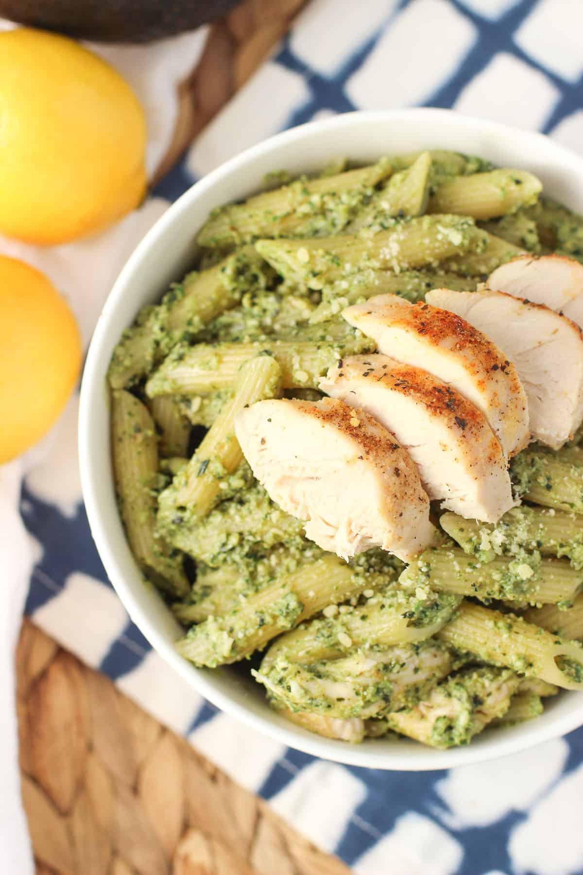 A bowl of pesto pasta with cooked chicken on top.