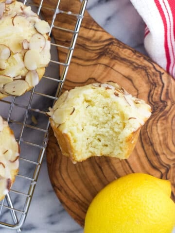 An overhead shot of a lemon ricotta muffin with a bite taken out of it on a small wooden serving board
