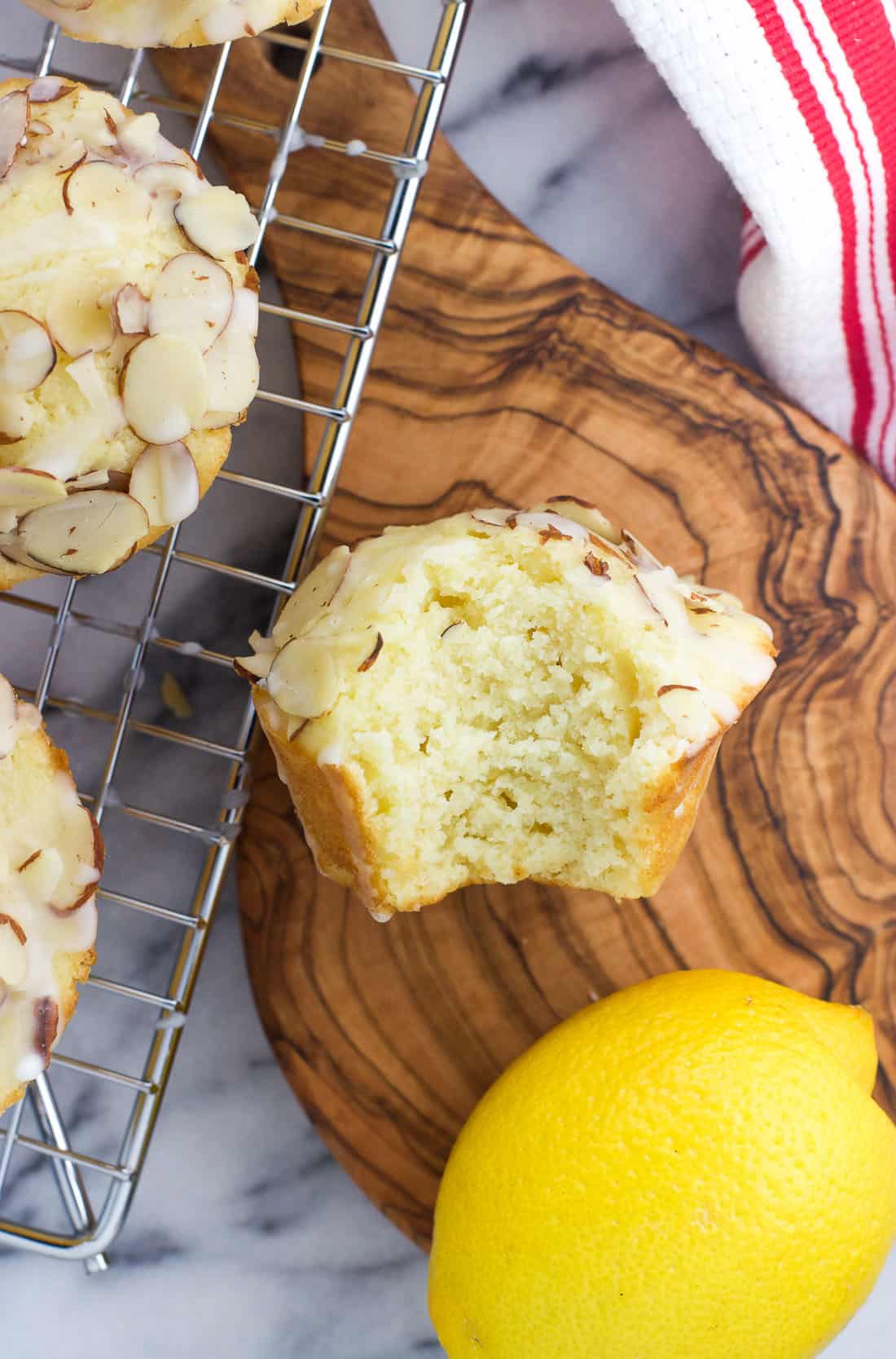 An overhead shot of a lemon ricotta muffin with a bite taken out of it on a small wooden serving board