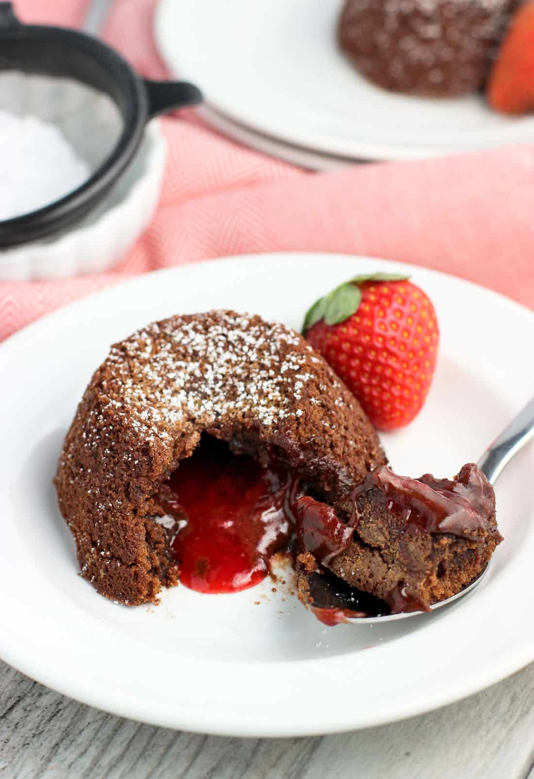 A big spoonful taken out of a lava cake, showing the strawberry filling oozing out.