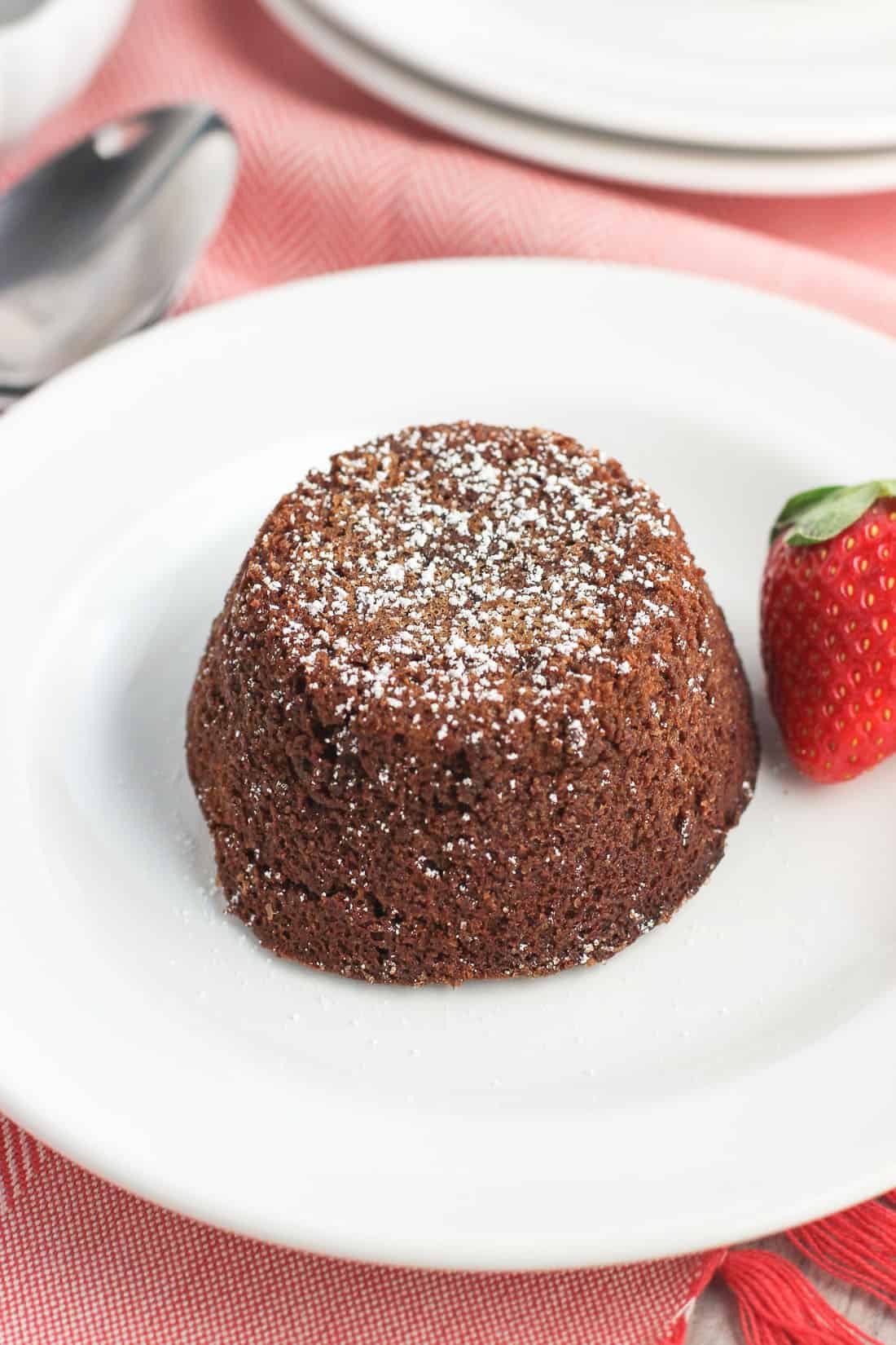 A whole lava cake inverted on a dessert plate, dusted with powdered sugar, and garnished with a fresh strawberry.