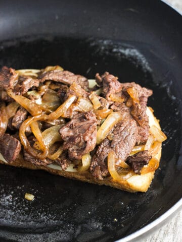 An open face cheesesteak panini in a skillet.