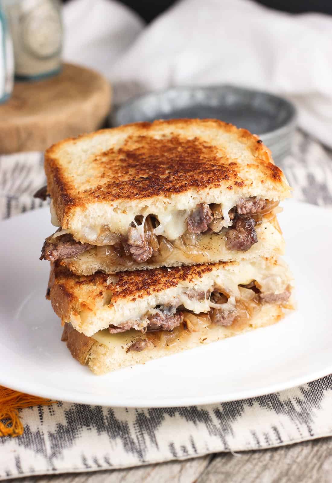 Two halves of a cheesesteak panini stacked on top of one another on a plate.