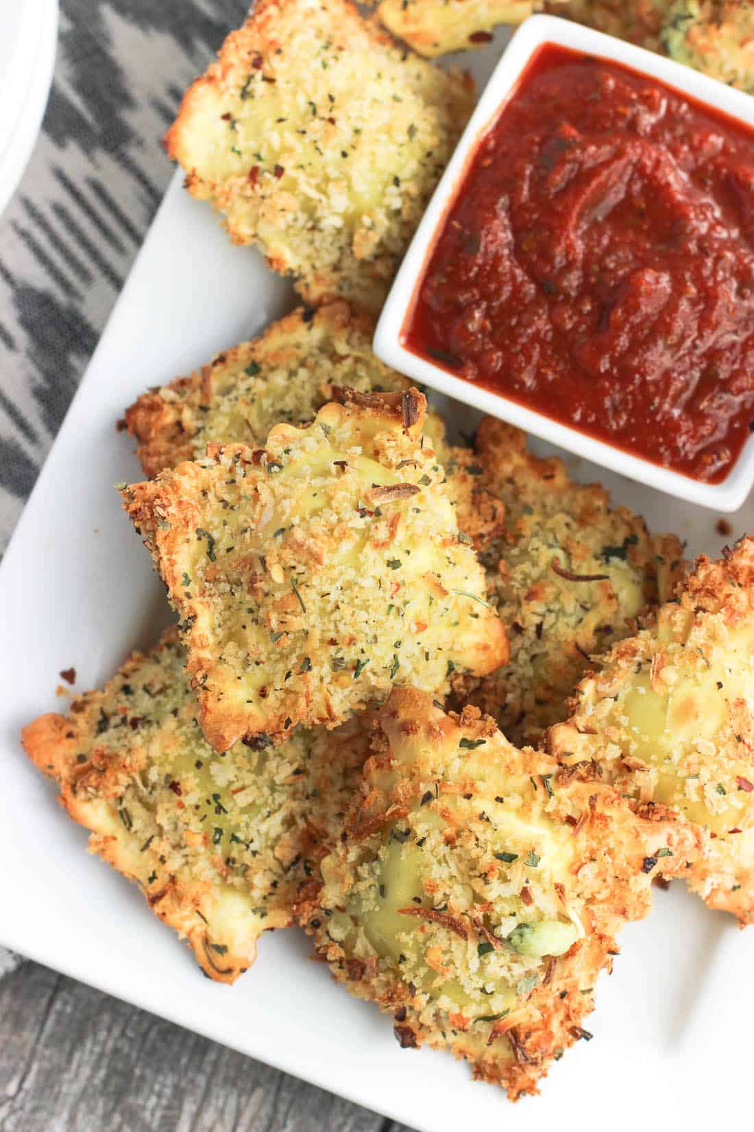 Toasted ravioli on a rectangular tray with a small bowl of marinara dipping sauce.