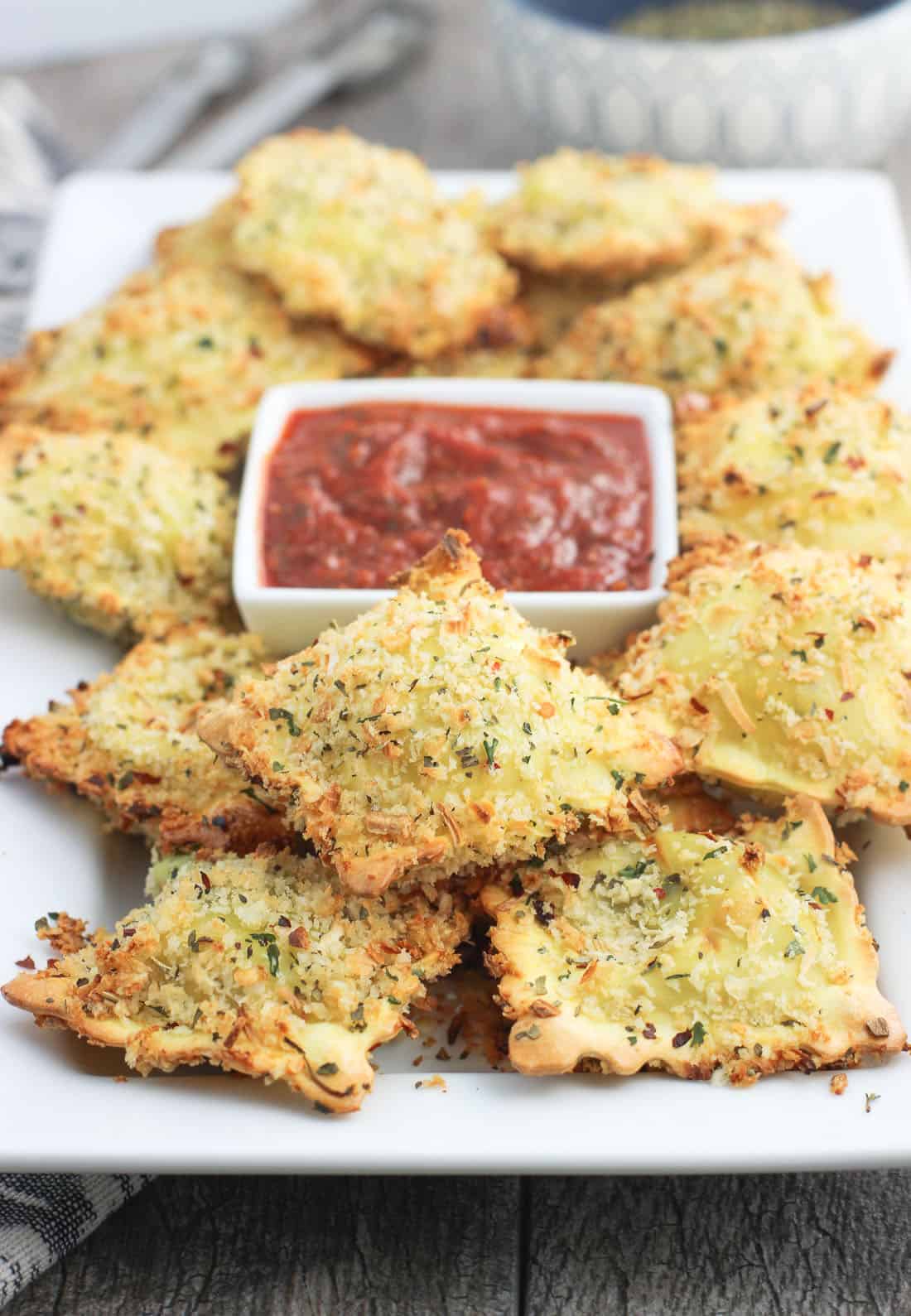 A rectangular serving dish of toasted ravioli with a bowl of marinara sauce in the middle.